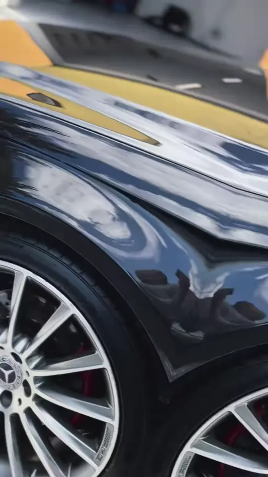 Čierny Mercedes kombi na štrku: lesklý blatník, koleso a bok, v laku sa zrkadlia stromy