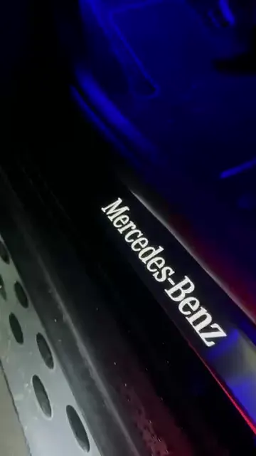 Interiér černého Mercedesu GLC v modrém osvětlení: práh s nápisem Mercedes-Benz, volant a dveře