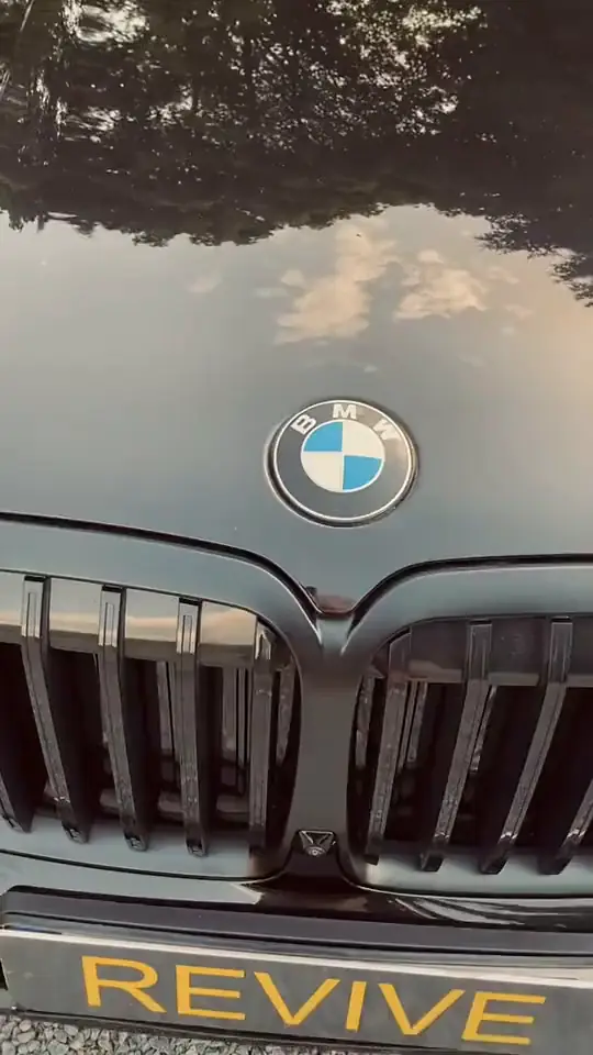 Černé BMW X7 se žlutou tabulkou REVIVE: logo na kapotě, maska a bok na štěrku před studiem