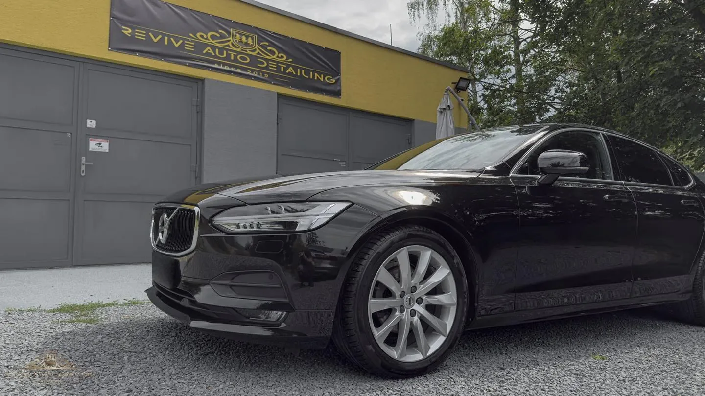 Black Volvo V90 in front of the studio, with a black banner with gold REVIVE AUTO DETAILING lettering above the grey gate
