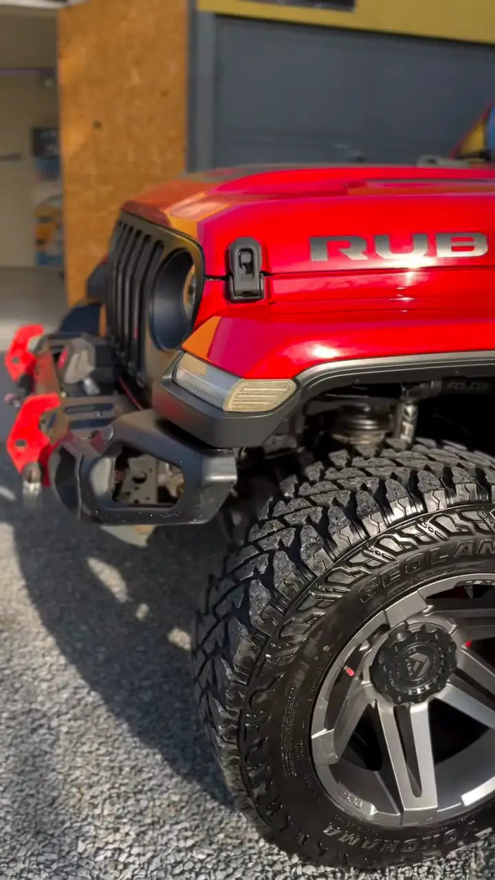 Red Jeep Wrangler Rubicon in front of the studio, a frame from our reel: grille, bonnet with the RUBICON lettering and a large off-road wheel